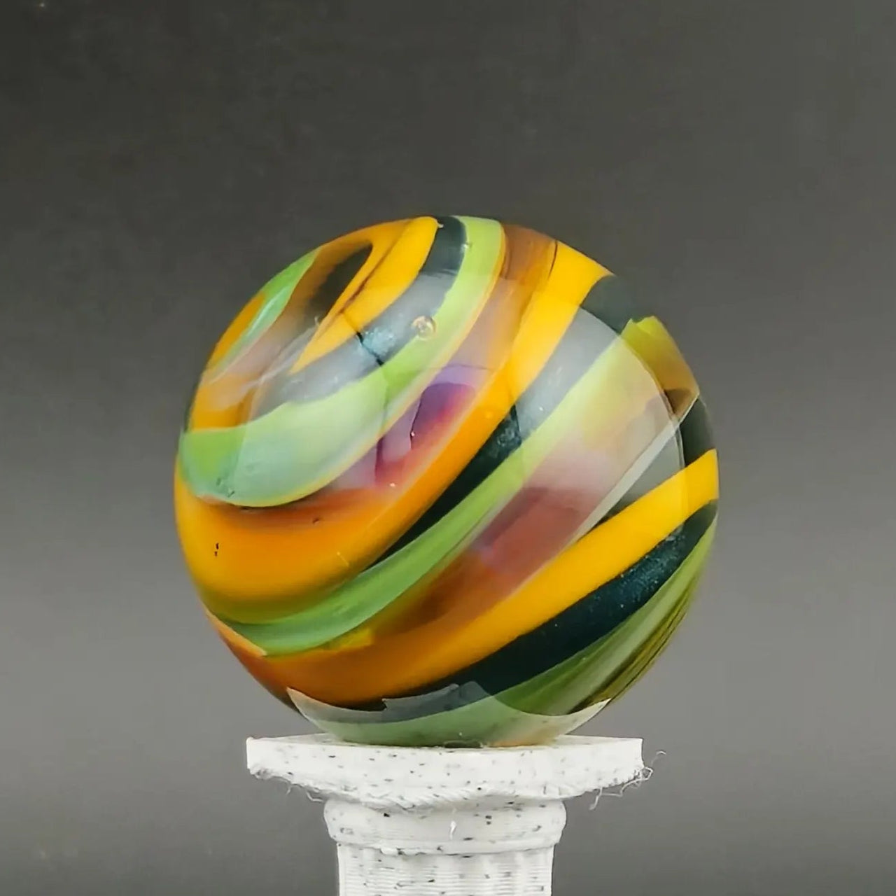 Colorful striped sphere on a white pedestal against a dark background