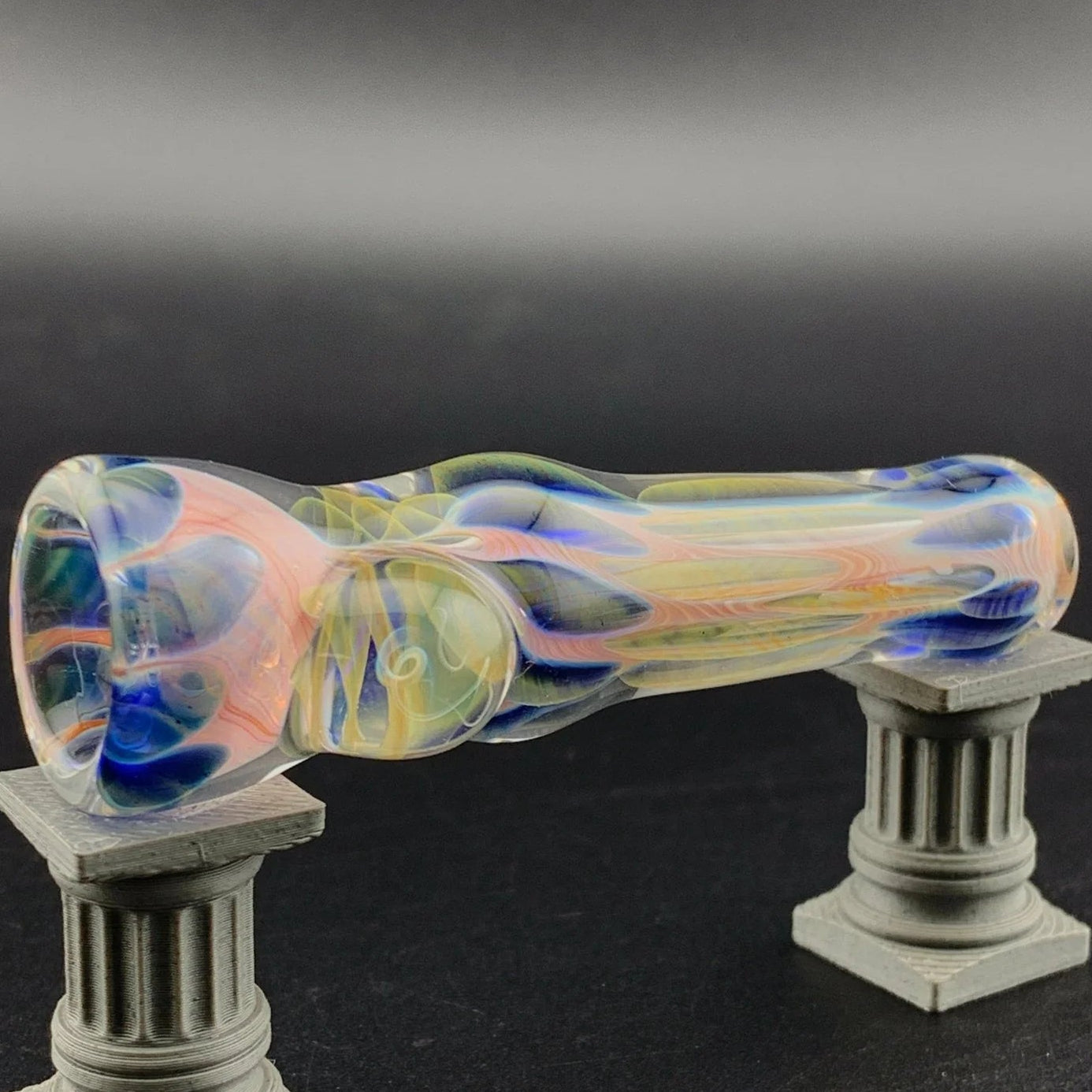 Colorful glass pipe on a decorative stand against a dark background